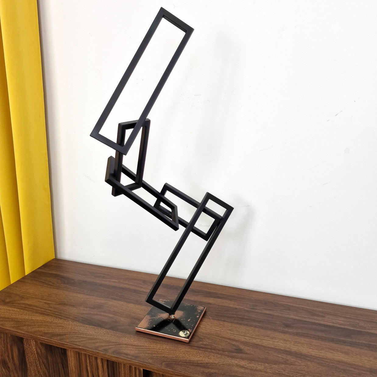 Escultura abstracta en metal negro sobre base de cobre, que representa el equilibrio entre forma y espacio negativo.