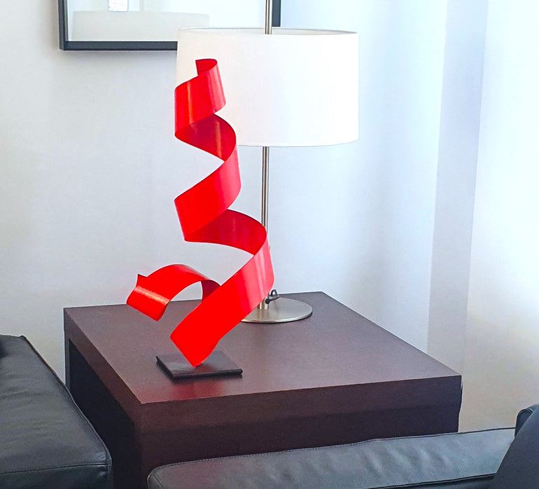 Escultura de mesa en espiral de metal rojo, obra contemporánea ideal para decorar espacios modernos con arte de autor. Diseño de José Soler sobre base oscura.