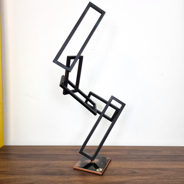 Escultura contemporánea en metal negro con estructuras rectangulares entrelazadas, ideal para interiores modernos.