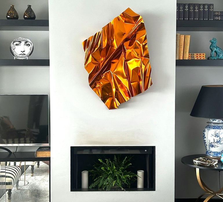 Escultura mural contemporánea en metal dorado con pliegues escultóricos, instalada sobre chimenea en salón de diseño moderno. Obra de arte de José Soler.